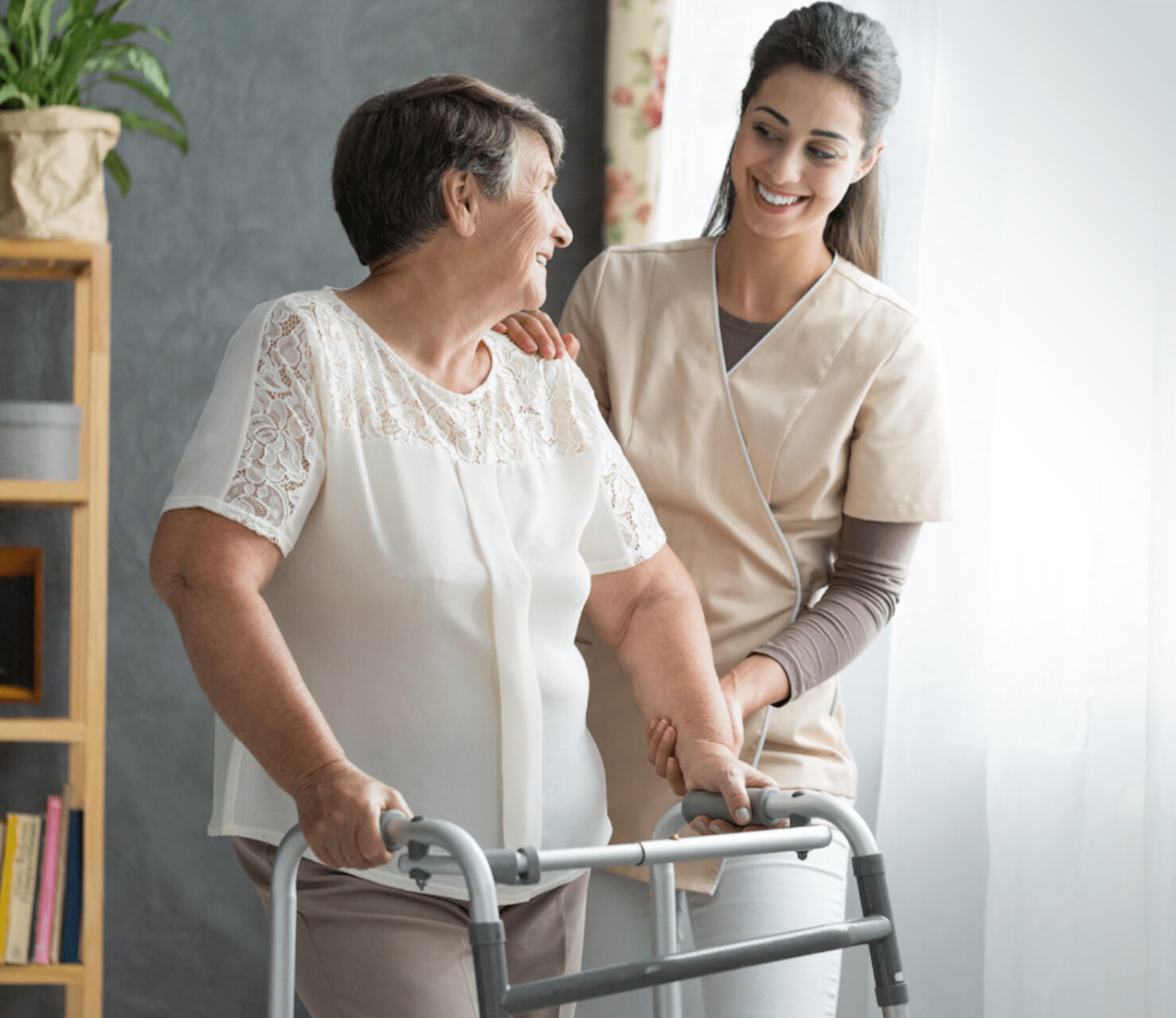 Glimlachende oudere vrouw die geholpen wordt door een lachende jongere vrouw met verpleegkleding